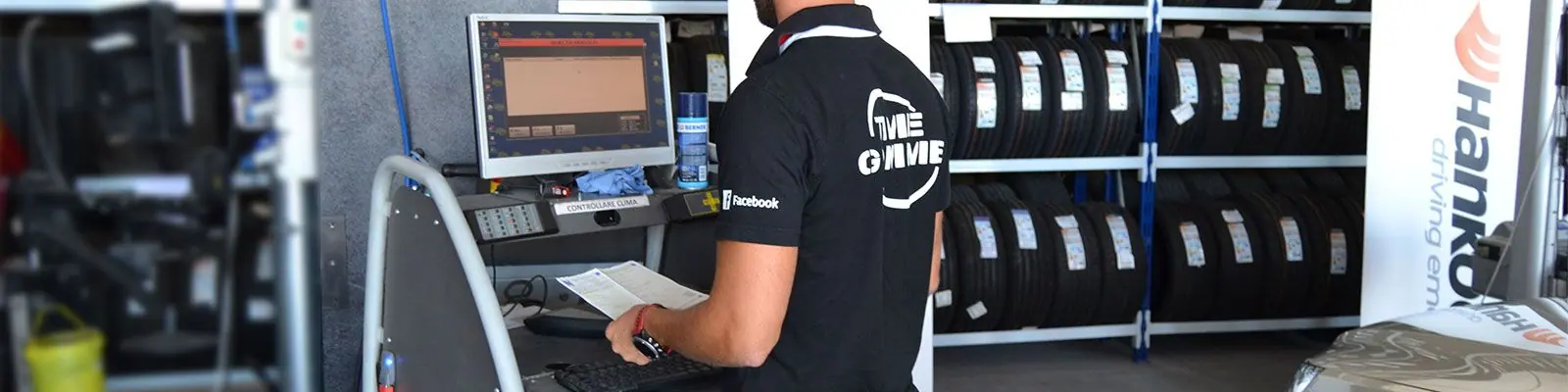 Un tecnico al computer in officina, con gli scaffali delle gomme sullo sfondo