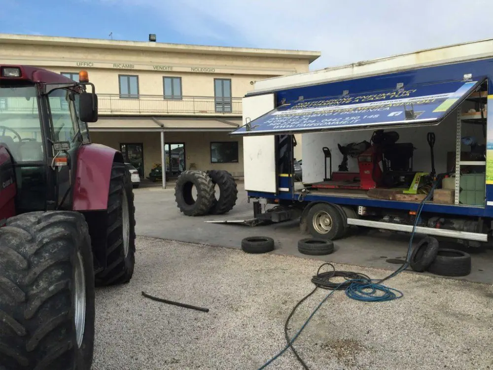 Un trattore rosso e l’autocarro di soccorso in un piazzale, con le gomme smontate
