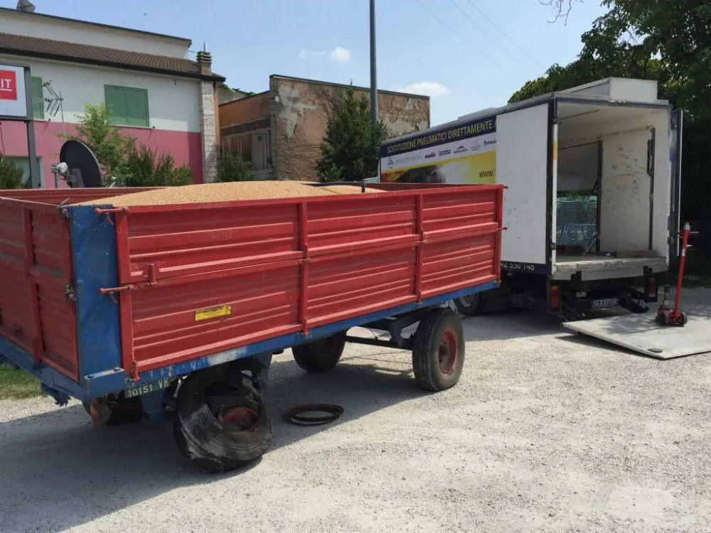 Un rimorchio agricolo rosso con la ruota smontata, accanto all’autocarro di soccorso