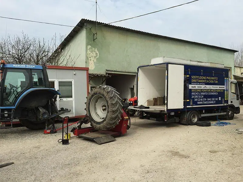 Un trattore blu e l’autocarro di soccorso davanti a un capannone